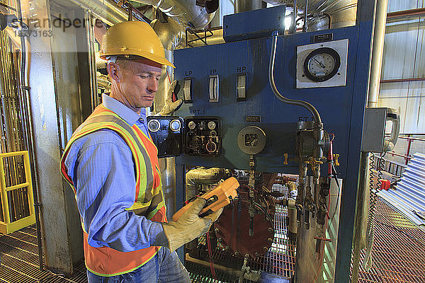 Arbeiter mit Schutzhelm und Warnweste  der ein Gerät mit Messgeräten und Monitoren benutzt