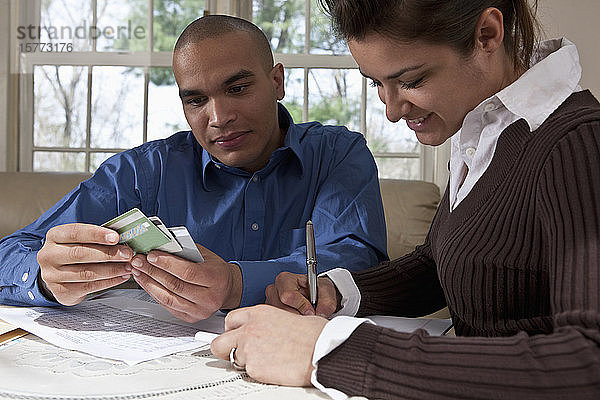 Ein junges Paar überprüft seine Finanzen an einem Tisch zu Hause mit Kreditkarten und Notizen