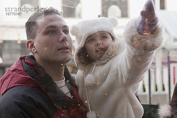 Zeit für den Vater und die kleine Tochter  während er sie im Arm hält und sie auf etwas in einem Fenster zeigt