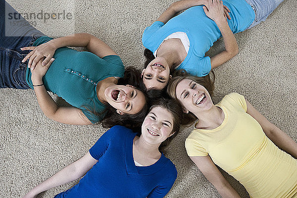 Porträt von vier Mädchen im Teenageralter  die zu Hause auf dem Boden sitzen und in die Kamera schauen