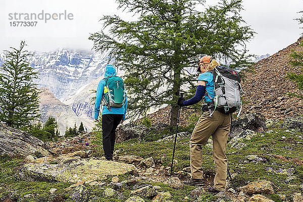 Zwei Wanderinnen auf einem felsigen Bergpfad mit einer wolkenverhangenen Bergkette im Hintergrund  Yoho National Park; Field  British Columbia  Kanada