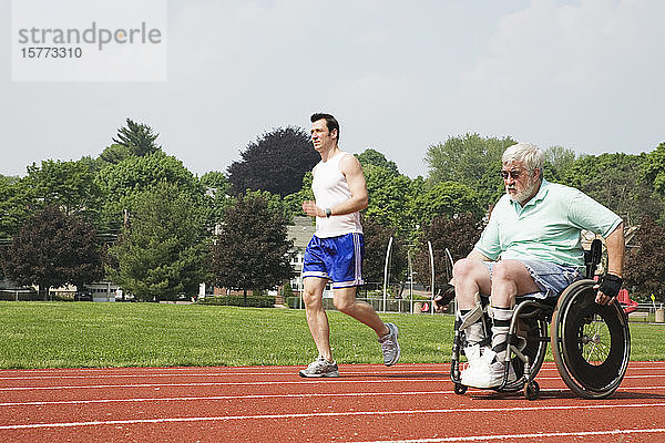 Junger Mann fährt mit einem behinderten älteren Mann auf der Rennbahn.