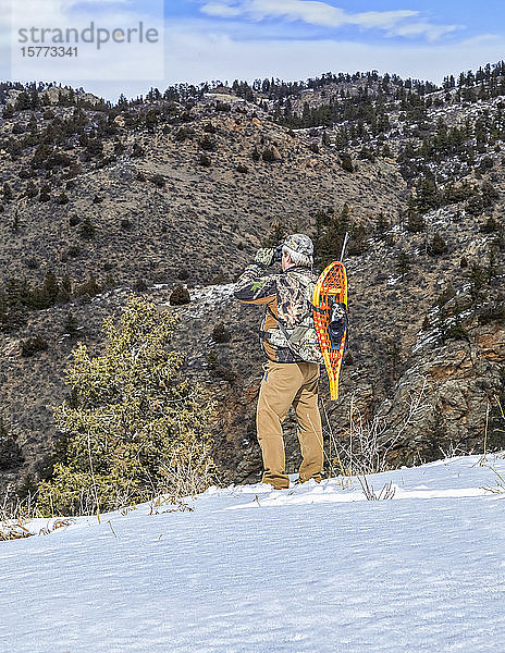 Jäger mit Schneeschuhen und Gewehr steht auf einem Hügel und schaut mit einem Fernglas hinaus; Denver  Colorado  Vereinigte Staaten von Amerika