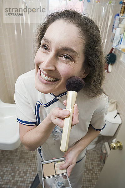Mittlere erwachsene Frau trägt Make-up auf ihr Gesicht auf und lächelt