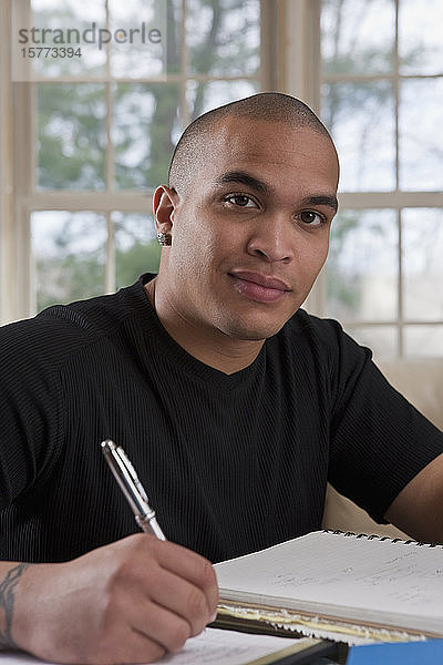 Männlicher Student sitzt zu Hause und macht sich Notizen in einem Notizbuch für Hausaufgaben