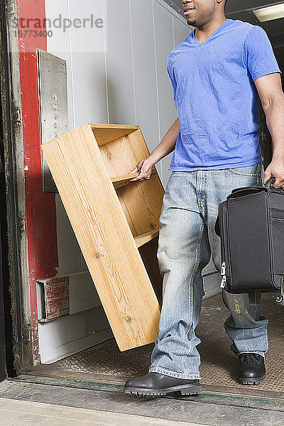 Junger Mann mit Koffer und Holzregal.