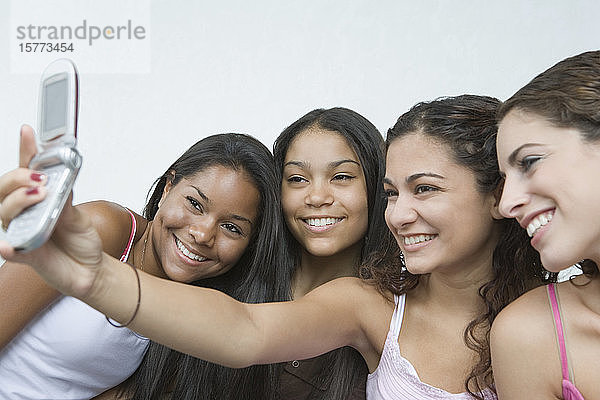 Nahaufnahme von vier Mädchen im Teenageralter  die sich mit einem Mobiltelefon fotografieren und lächeln