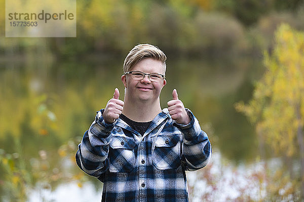 Ein junger Mann mit Down-Syndrom zeigt an einem warmen Herbstabend in einem Stadtpark den Daumen nach oben: Edmonton  Alberta  Kanada