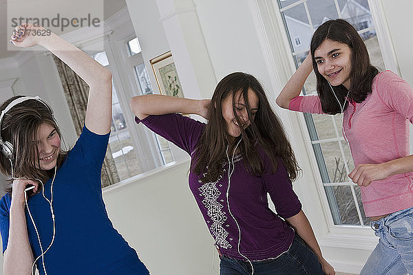 Drei Mädchen im Teenageralter feiern eine Tanzparty  während sie mit Kopfhörern Musik hören