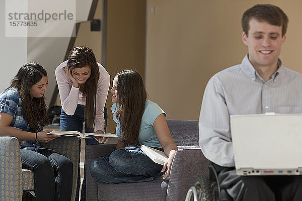 College-Studenten lernen in einem Gemeinschaftsraum mit einem männlichen Studenten im Rollstuhl im Vordergrund
