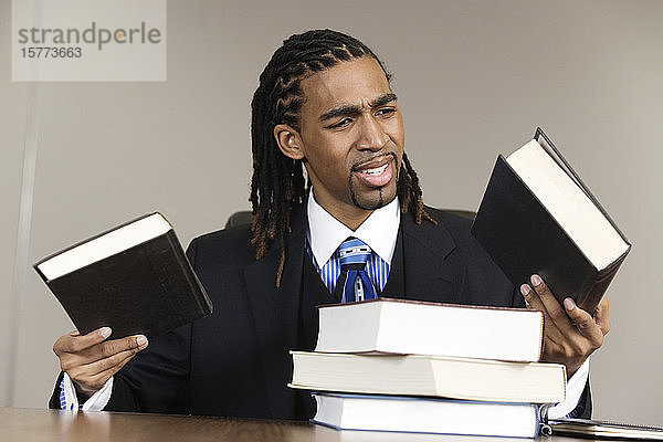 Ein verwirrter junger Geschäftsmann hält Bücher in einem Büro.