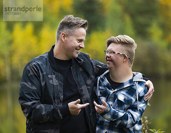 Ein junger Mann mit Down-Syndrom und sein Vater genießen an einem warmen Herbstabend in einem Stadtpark die Gesellschaft des anderen und machen sich gegenseitig lustige Gesten: Edmonton  Alberta  Kanada