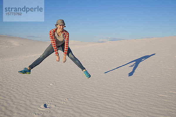 Eine junge Frau springt in die Luft auf dem weißen Sand mit blauem Himmel  White Sands National Monument; Alamogordo  New Mexico  Vereinigte Staaten von Amerika