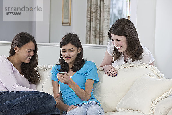 Drei Mädchen im Teenageralter hängen zu Hause zusammen ab und hören Musik über ein kleines tragbares Gerät