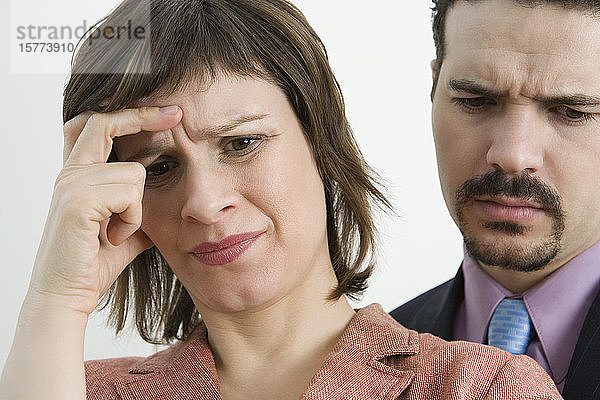 Nahaufnahme einer Geschäftsfrau  die unter Kopfschmerzen leidet  mit einem Geschäftsmann hinter ihr