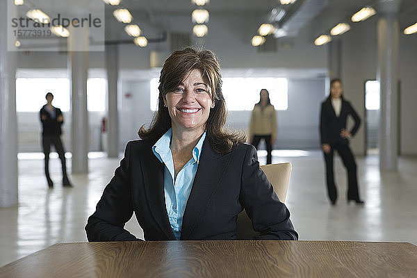Porträt einer lächelnden Geschäftsfrau mit Menschen im Hintergrund.