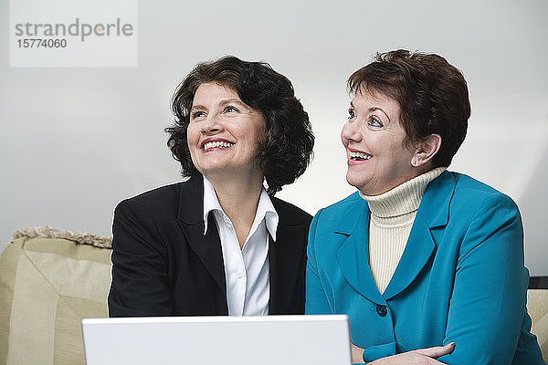 Blick auf lächelnde Geschäftsfrauen  die vor einem Laptop sitzen.