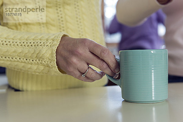 Mittelteil einer reifen Frau mit Tasse in der Küche.