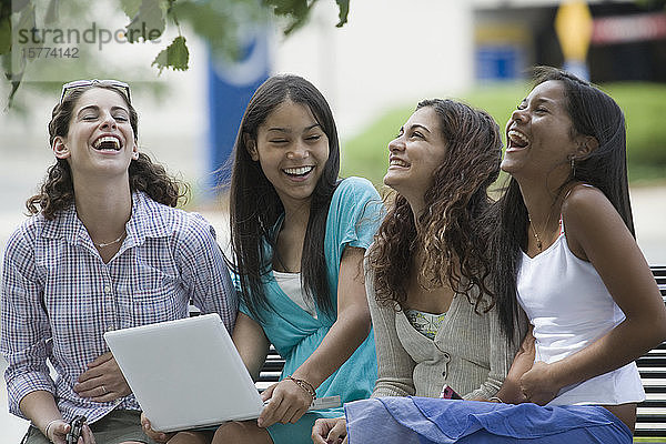 Vier Mädchen im Teenageralter sitzen auf einer Bank und lächeln auf dem Schulcampus