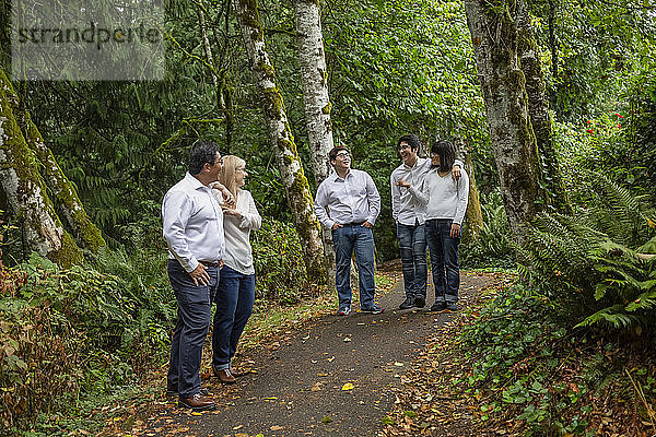 Familie  die auf einem Weg in einem Park mit Wald spazieren geht und sich unterhält; Langley  British Columbia  Kanada