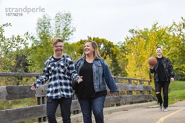Ein junger Mann mit Down-Syndrom geht mit seinem Vater und seiner Mutter an einem warmen Herbstabend in einem Stadtpark spazieren und genießt die Gesellschaft des anderen: Edmonton  Alberta  Kanada