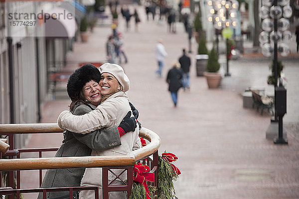 Zwei Frauen umarmen sich  während sie auf einem weihnachtlich geschmückten Balkon stehen und auf die Stadt hinausschauen; Boston  Massachusetts  Vereinigte Staaten von Amerika