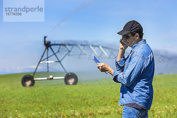 Landwirt mit Tablet und Smartphone auf einem Feld mit Bewässerung; Alberta  Kanada