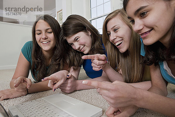 Vier Mädchen im Teenageralter benutzen einen Laptop und zeigen lachend auf den Bildschirm