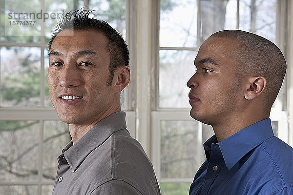 Porträt der Seitenansicht von zwei jungen Geschäftsleuten  die nach links blickend stehen  einer schaut in die Kamera