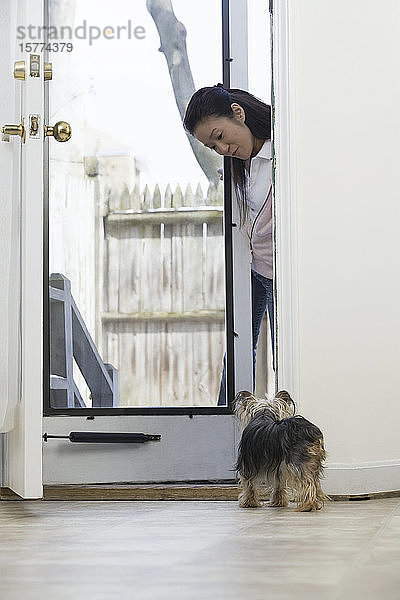 Junge Frau betrachtet einen Yorkshire Terrier durch eine Tür