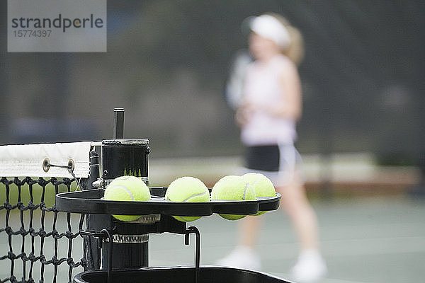 Nahaufnahme von Tennisbällen mit einer Frau  die im Hintergrund Tennis spielt