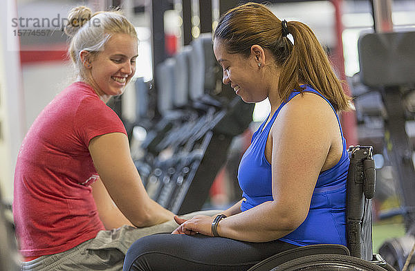 Junge Frau im Rollstuhl im Gespräch mit einer anderen jungen Frau in einem Fitnessclub