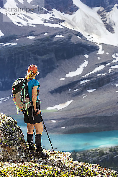 Wanderin auf felsigem Grat mit Blick auf einen blauen Alpensee und eine schneebedeckte Felswand in der Ferne  Yoho National Park; Field  British Columbia  Kanada