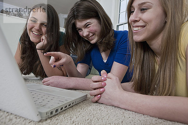 Drei Mädchen im Teenageralter benutzen einen Laptop und zeigen lachend auf den Bildschirm