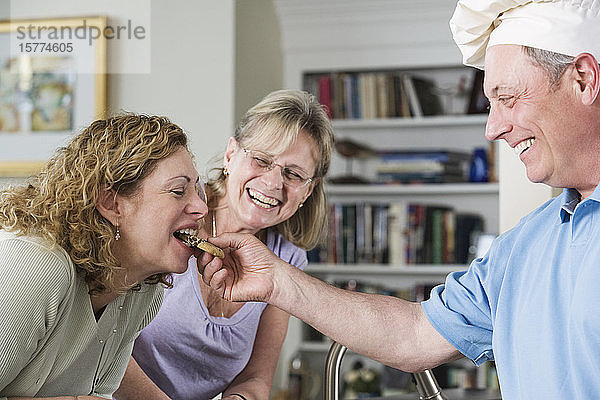 Älterer Mann füttert eine Frau zu Hause mit Keksen.