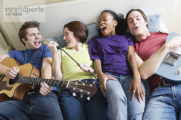 Zwei Männer und zwei Frauen liegen mit Gitarren und Mikrofon auf einem Bett.