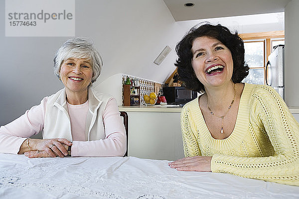 Zwei fröhliche Frauen sitzen an einem Esstisch.