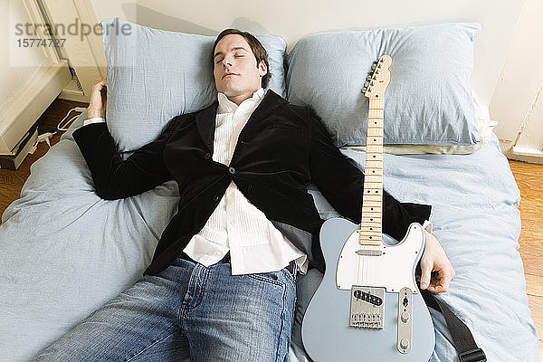 Schlafender Mann im Bett mit Gitarre.