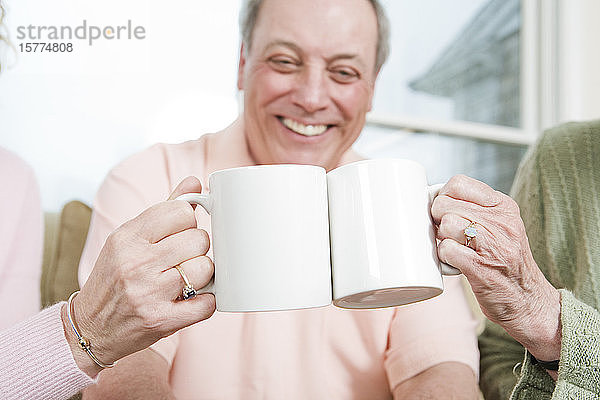 Älterer Mann lächelt mit zwei Frauen  die Kaffeetassen im Vordergrund halten.