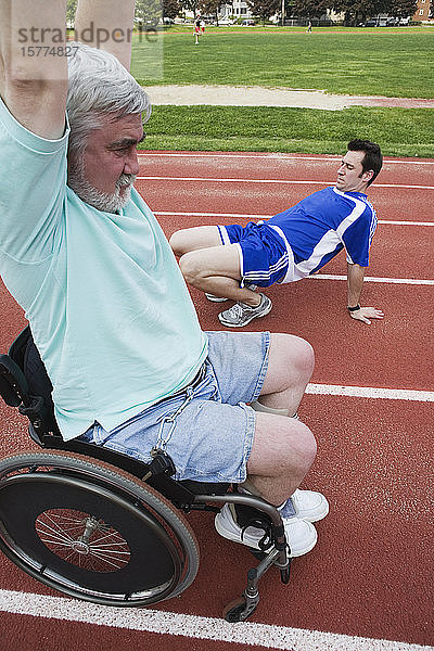 Junger Mann und ein behinderter älterer Mann trainieren auf einer Rennbahn.
