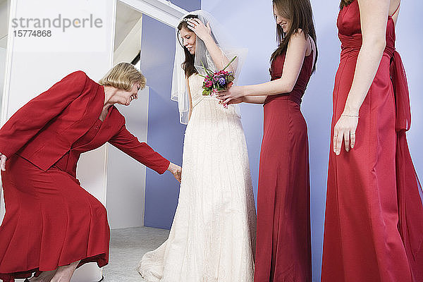 Junge Braut steht mit Brautjungfern  während die Mutter das Kleid zurechtrückt.