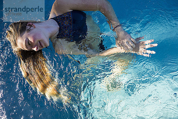 Ein junges Mädchen in einem Swimmingpool  ihr langes blondes Haar fächelt sich im Wasser auf.