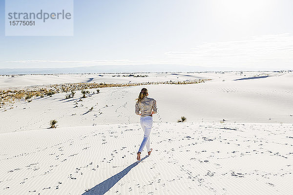 Ein junges Mädchen steht und schaut auf eine weite offene Fläche mit Sanddünen.