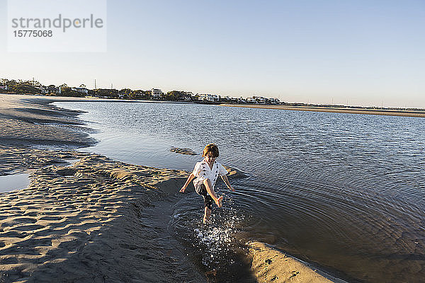 Ein sechsjähriger Junge am Strand  der im flachen Wasser planscht