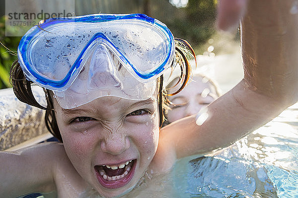 Ein Junge mit Brille  der vor der Kamera lacht  in einem warmen Schwimmbad mit seiner Schwester.