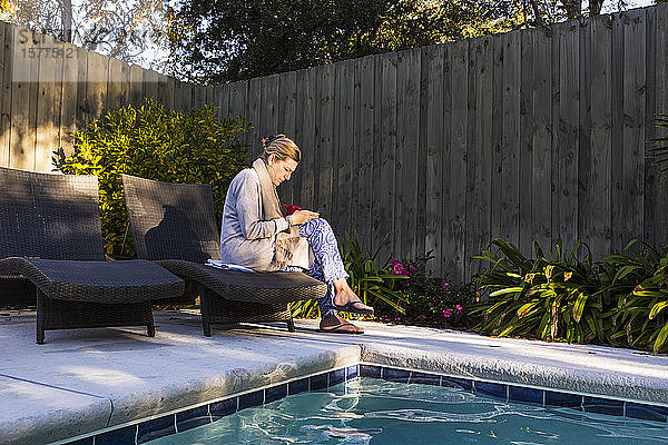 Frau sitzt auf einer Sonnenliege an einem Swimmingpool