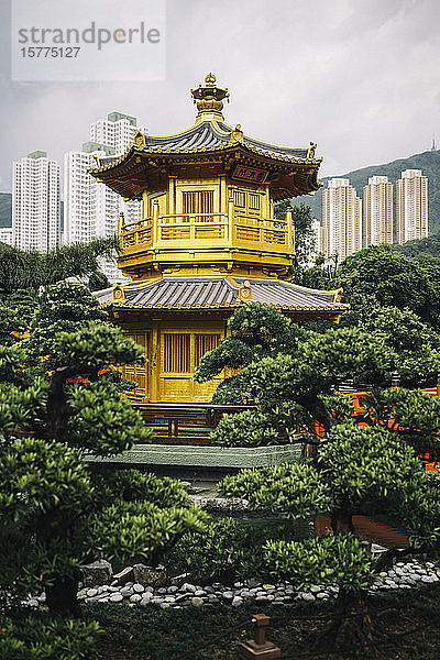 Außenansicht eines von Bäumen umgebenen goldenen Tempels  im Hintergrund Wolkenkratzer.