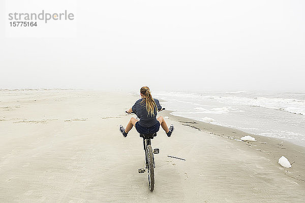 Teenagerin beim Fahrradfahren auf Sand am Strand