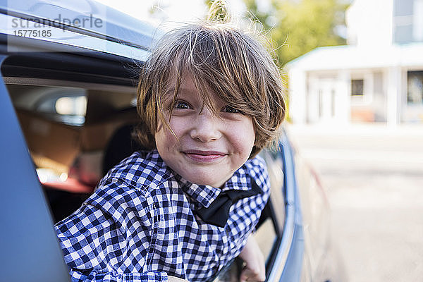Ein sechsjähriger Junge lächelt in die Kamera und schaut aus dem Autofenster