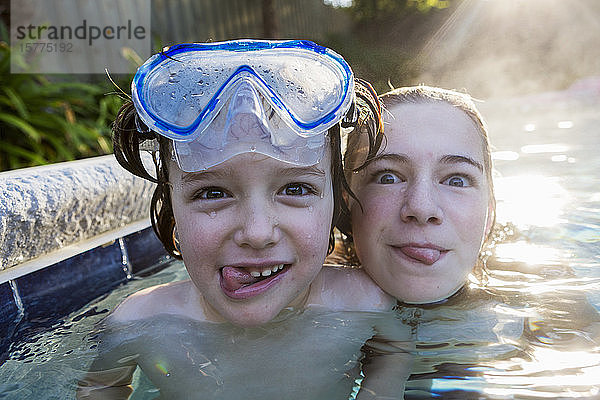Ein jugendliches Mädchen und ein Bruder in einem warmen Pool  die in die Kamera schauen und ihre Zungen herausstrecken.